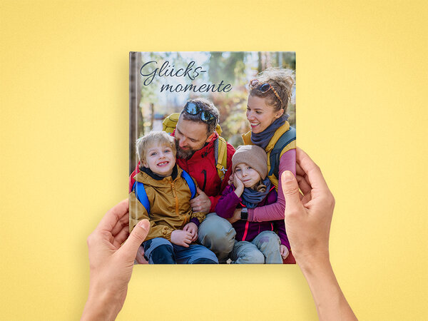 Zwei Hände halten ein Fotobuch im A4-Hochformat. Auf dem Cover ist eine Familie in Wanderkleidung abgebildet.
