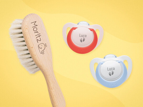 Babyhaarbürste mit Namensgravur und Emoji. Daneben zwei weiße Schnuller mit rotem oder hellblauem Farbakzent und Gravur.