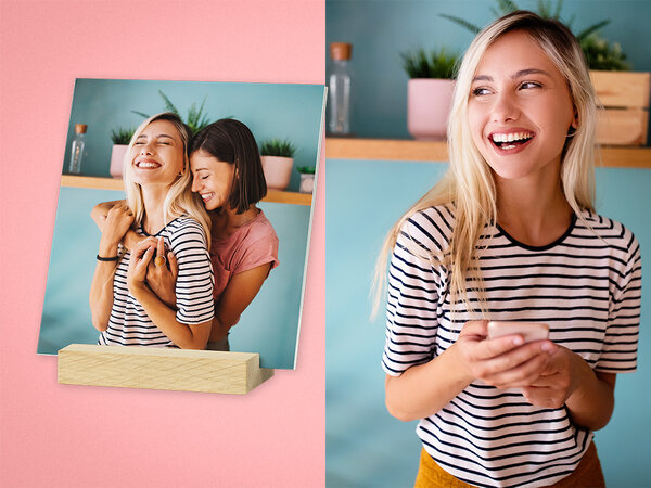 Mehrere quadratische Fotos stehen frei in einem Holzstandfuß. Das vorderste Foto zeigt zwei Frauen, die sich umarmen.